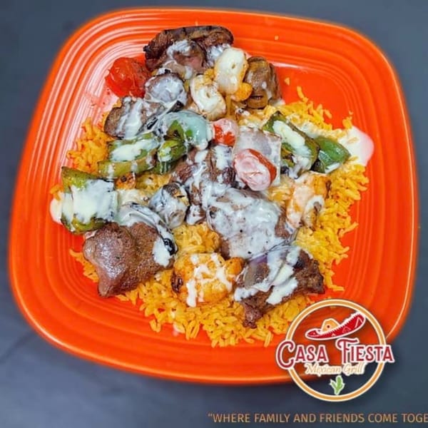 Casa Fiesta Mexican Grill's steak and vegetable skewers with white sauce over yellow rice on an orange plate.