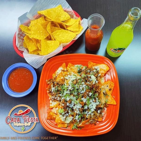 Nachos with meat, cheese, onions, and cilantro, alongside chips, salsa, and a Jarritos soda.
