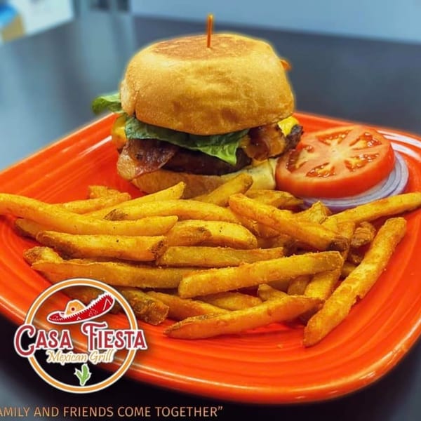 A Casa Fiesta Mexican Grill burger with fries, tomato, and onion on an orange plate.
