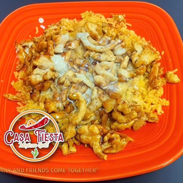 Casa Fiesta's chicken and rice dish, topped with a creamy sauce, served on an orange plate.