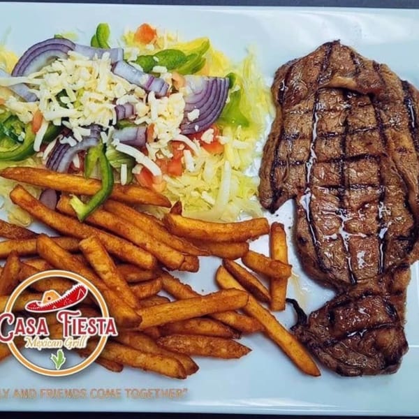 Grilled steak with fries and a side salad topped with cheese, onions, and peppers.