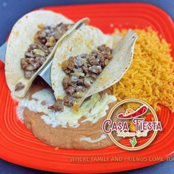 Two beef tacos with melted cheese, refried beans, and yellow rice on a red plate.