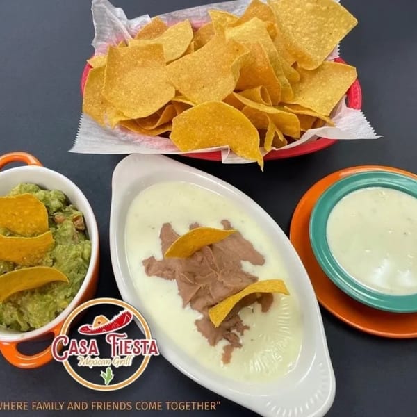 A basket of tortilla chips, a bowl of guacamole, and two bowls of queso dip from Casa Fiesta.